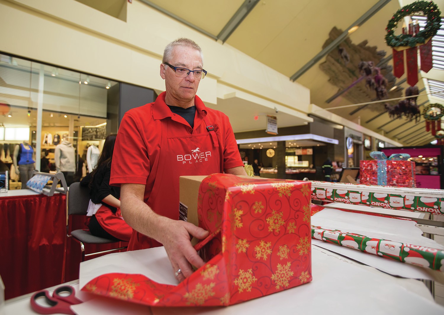 WRAPPING AWAY - Volunteer Serge Gingras measured out wrapping paper for a customer’s gift at the gift wrapping station at Bower Place Shopping Centre earlier this week. All the proceeds from the gift wrapping go towards Women’s Outreach.