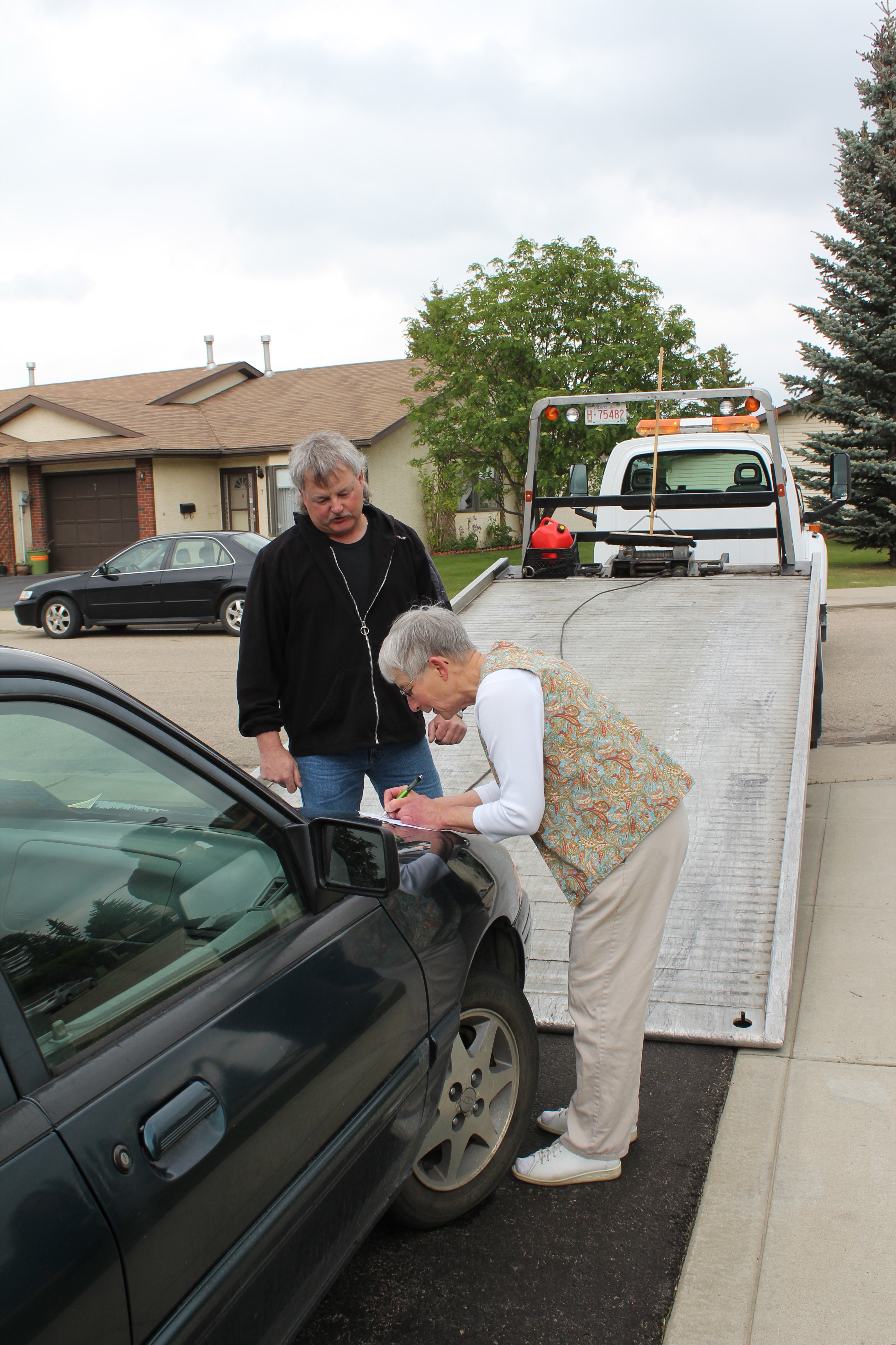 RIDE ON – A tow truck driver from DLJ’s Haulaway Ltd. watches as Rene Neumann signs her car over to him. Neumann is the first person to donate a vehicle to the Kidney Foundation here in Red Deer.