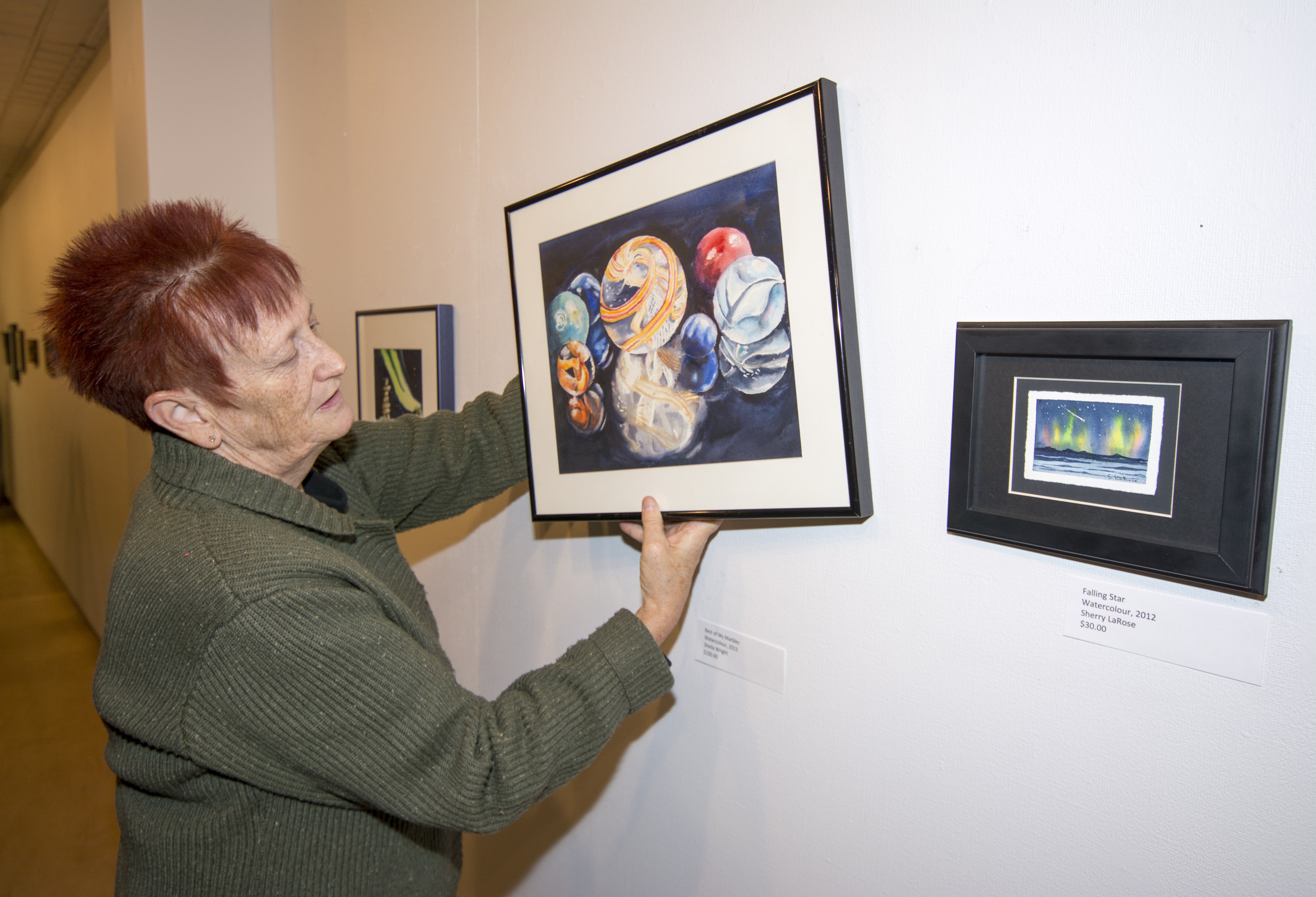PREPARING – Diana Anderson of the Red Deer Arts Council puts the finishing touches on a new exhibit featuring Council members’ works of art in the Kiwanis Gallery.