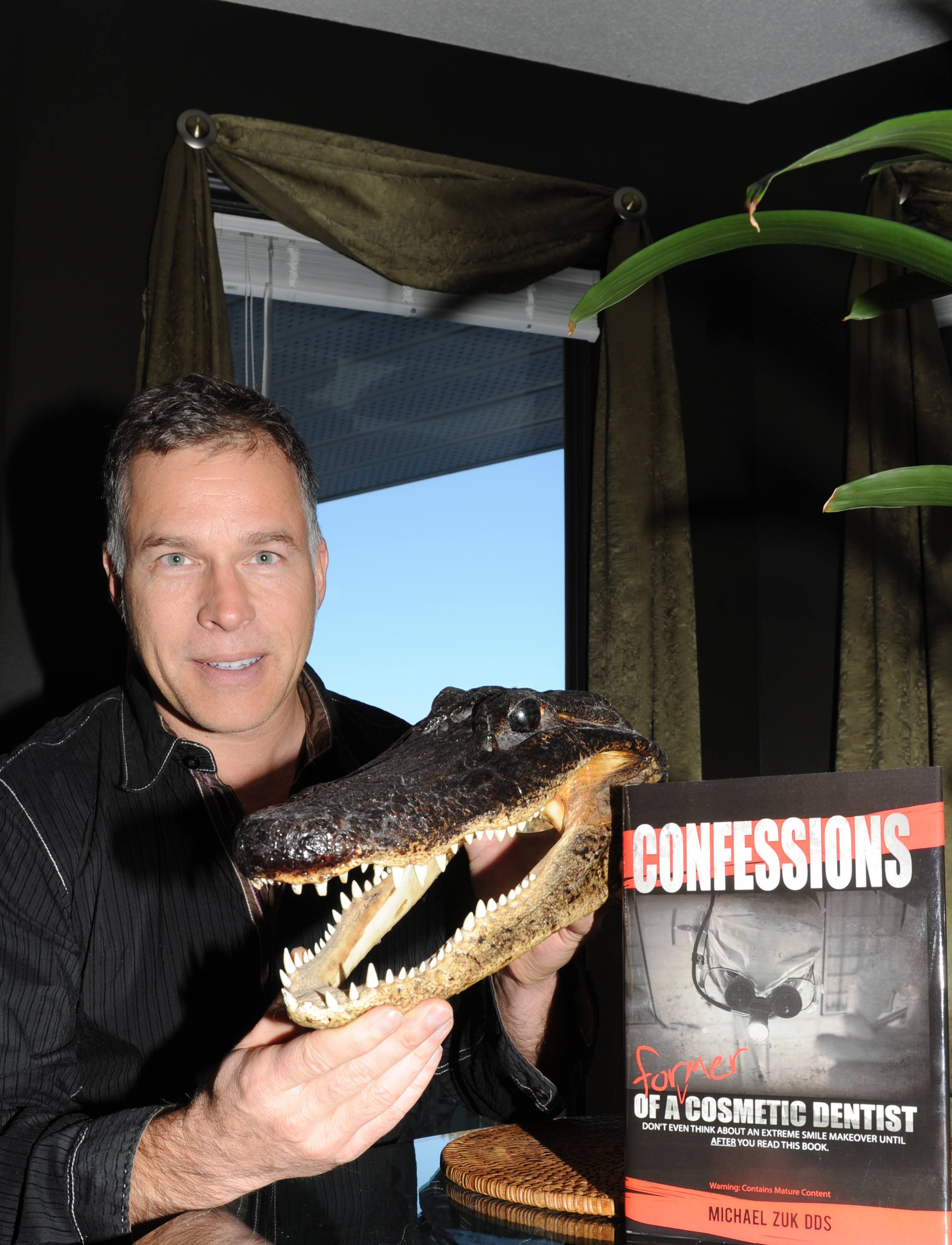 COLLECTION- Teeth collector and local dentist Dr. Michael Zuk holds up an alligator head complete with a set of chompers as well as his book Confessions of a Former Cosmetic Dentist.