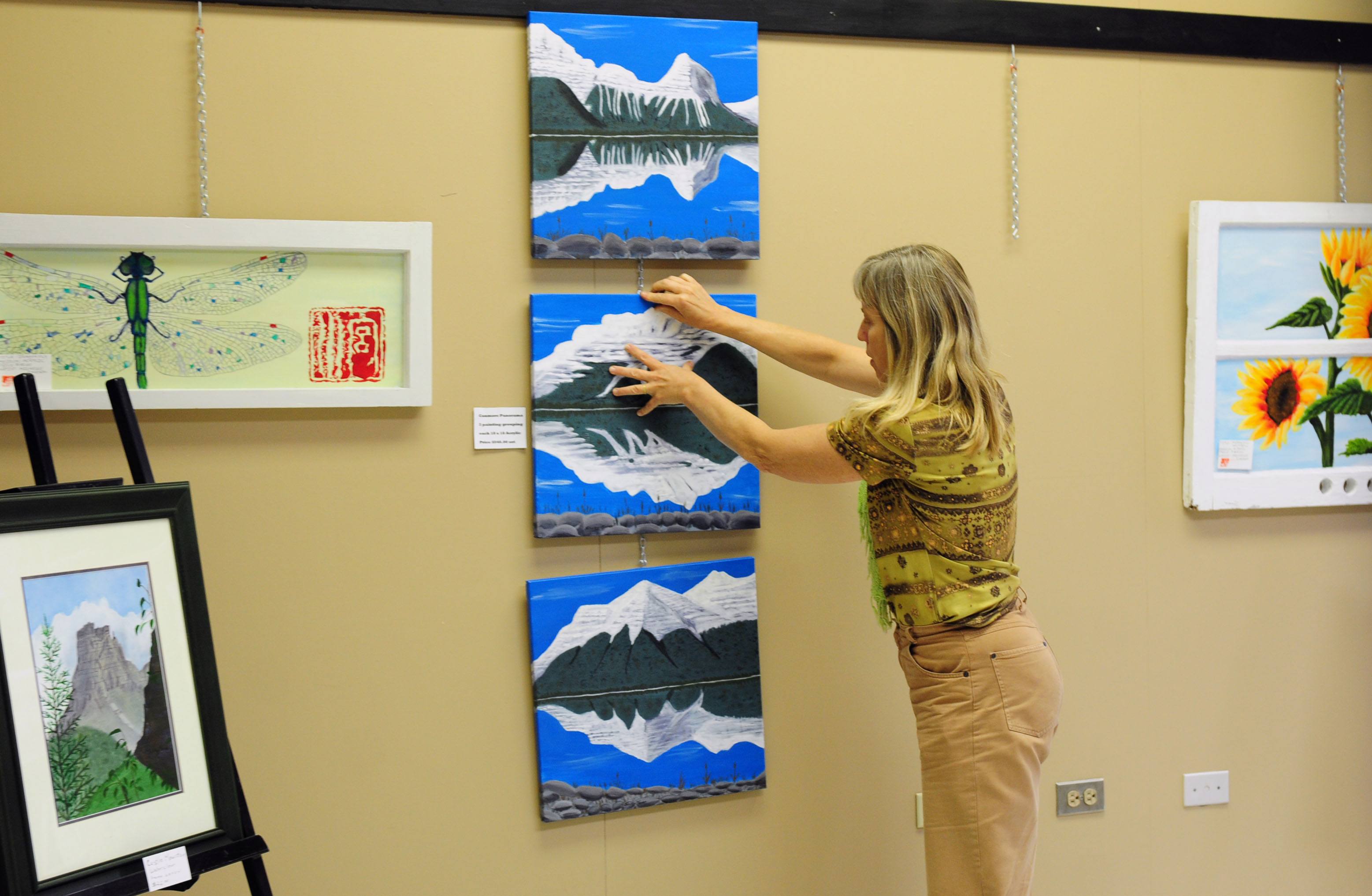 HANGING- Bev Randers hangs up some of the art by local artists at the Hub on Ross St. recently.