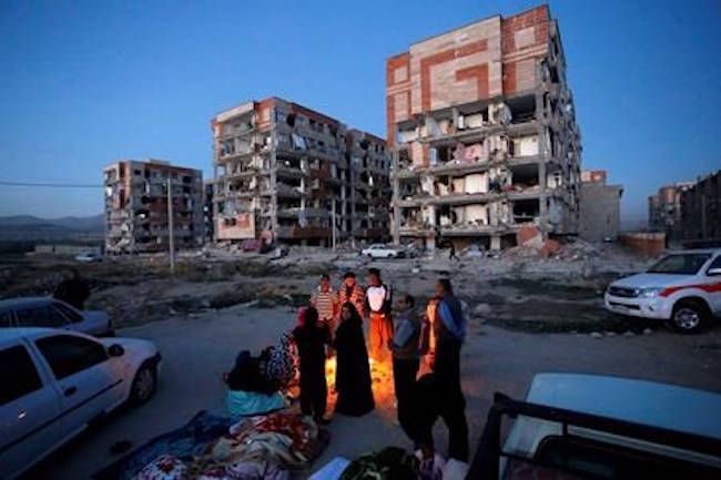 In this photo provided by the Iranian Students News Agency, ISNA, survivors of the earthquake warm themselves in front of destroyed buildings at the city of Sarpol-e-Zahab in western Iran, Monday, Nov. 13, 2017. (Pouria Pakizeh/ISNA via AP)