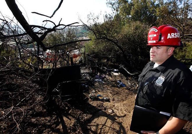 Los Angeles Fire Department Fire Arson Counter-Terrorism investigator Angel Alvarez checks a burned out homeless camp after a brush fire erupted in hills in Elysian Park in Los Angeles Thursday, Dec. 14, 2017. (AP Photo/Damian Dovarganes)