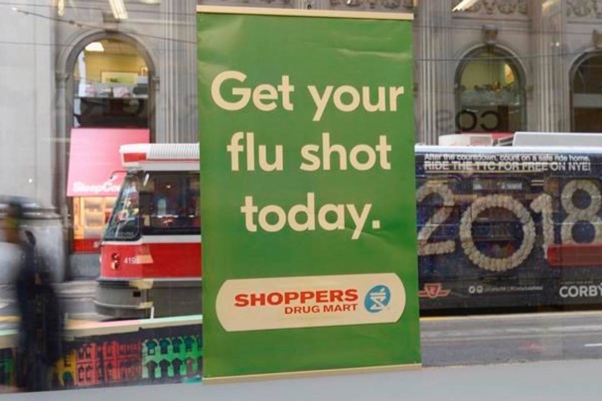 A man walks pass a sign for flu shots in Toronto. (Doug Ives/The Canadian Press)