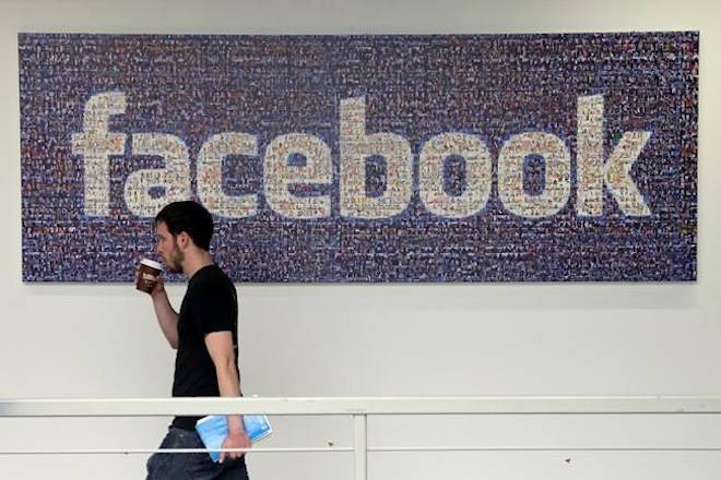 FILE - In this March 15, 2013, file photo, a Facebook employee walks past a sign at Facebook headquarters in Menlo Park, Calif. (AP Photo/Jeff Chiu, File)