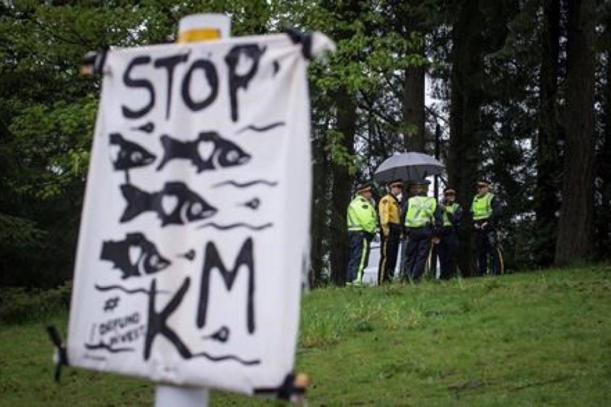 RCMP officers gather nearby as protesters opposed to the Kinder Morgan Trans Mountain Pipeline expansion defy a court order and block a gate at the company’s facility, in Burnaby, B.C., on Saturday April 28, 2018. (Darryl Dyck/The Canadian Press)