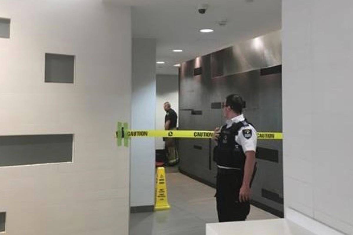 A security guard stands by as firefighters inspect a wall in the women’s washroom in the Core Shopping Centre in Calgary on Monday. (Lauren Krugel/The Canadian Press)