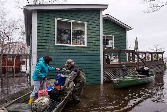 Residents carry groceries and clothes out of canoes as floodwaters surround a home on Grand Lake in New Brunswick on Tuesday, May 1, 2018. THE CANADIAN PRESS/Darren Calabrese