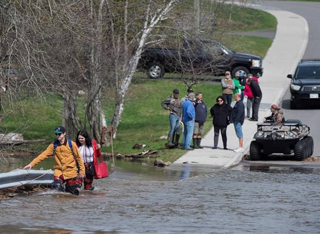 Simon Barton, left, and Chelsea Burley wear make shift waders of garbage bags and packing tape as they cross a flooded road in Saint John, N.B. on Sunday, May 6, 2018. THE CANADIAN PRESS/Andrew Vaughan
