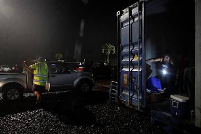 Volunteer Chasity Quihano, right, uses a flashlight to sort donated goods in a container at a makeshift donation center, Tuesday, May 8, 2018, in Pahoa, Hawaii. Hawaii County officials have issued a cellphone alert warning residents of a subdivision to immediately evacuate after two new lava fissures opened in a neighboring community. (AP Photo/Jae C. Hong)