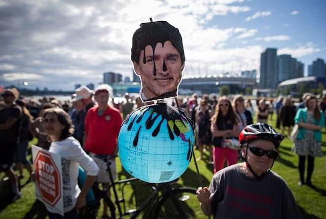 A protester holds a photo of Prime Minister Justin Trudeau and a representation of the globe covered in oil during a protest against the Kinder Morgan Trans Mountain Pipeline expansion in Vancouver, B.C., on Tuesday May 29, 2018. The federal Liberal government is spending $4.5 billion to buy Trans Mountain and all of Kinder Morgan Canada’s core assets, Finance Minister Bill Morneau said Tuesday as he unveiled the government’s long-awaited, big-budget strategy to save the plan to expand the oilsands pipeline. THE CANADIAN PRESS/Darryl Dyck