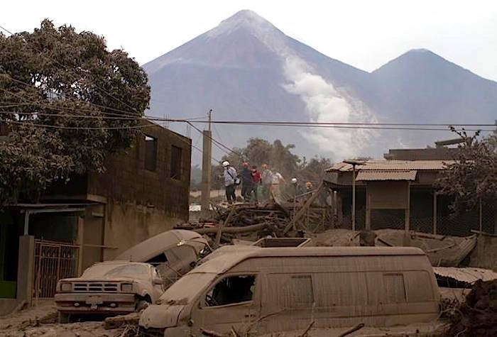 Rescue workers walk on rooftops in Escuintla, Guatemala, Monday, June 4, 2018, blanketed with heavy ash spewed by the Volcan de Fuego, or “Volcano of Fire,” pictured in the background, left center. A fiery volcanic eruption in south-central Guatemala sent lava flowing into rural communities, killing at least 25 as rescuers struggled to reach people where homes and roads were charred and blanketed with ash. (AP Photo/Luis Soto)