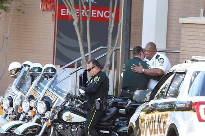 A Orange County Sheriff Motor deputy,center, gives support to a Orlando Police Motor officer,right, at Orlando Regional Medical Center after a OPD officer was shot and severely injured while responding over night to a domestic dispute call Monday, June 10, 2018. (Red Huber /Orlando Sentinel via AP)