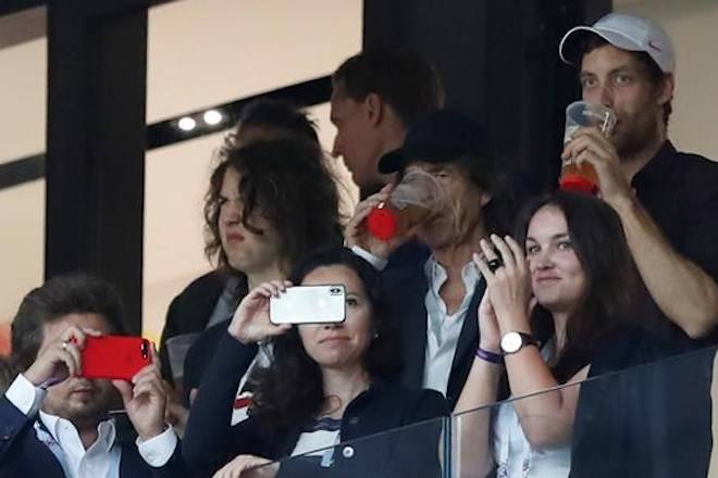 Singer Mick Jagger of the Rolling Stones, in black baseball hat, drinks a pint during the semifinal match between Croatia and England at the 2018 soccer World Cup in the Luzhniki Stadium in, Moscow, Russia, Wednesday, July 11, 2018. (AP Photo/Alastair Grant)