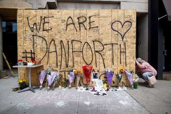 A woman writes a message on a makeshift memorial remembering the victims of a shooting on Sunday evening on Danforth Avenue, in Toronto on Tuesday, July 24, 2018. THE CANADIAN PRESS/Mark Blinch