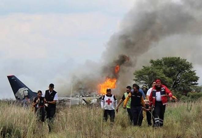 In this photo released by Red Cross Durango communications office, Red Cross workers and rescue workers carry an injured person on a stretcher, right, as airline workers, left, walk away from the site where an Aeromexico airliner crashed in a field near the airport in Durango, Mexico, Tuesday, July 31, 2018. (Red Cross Durango via AP)