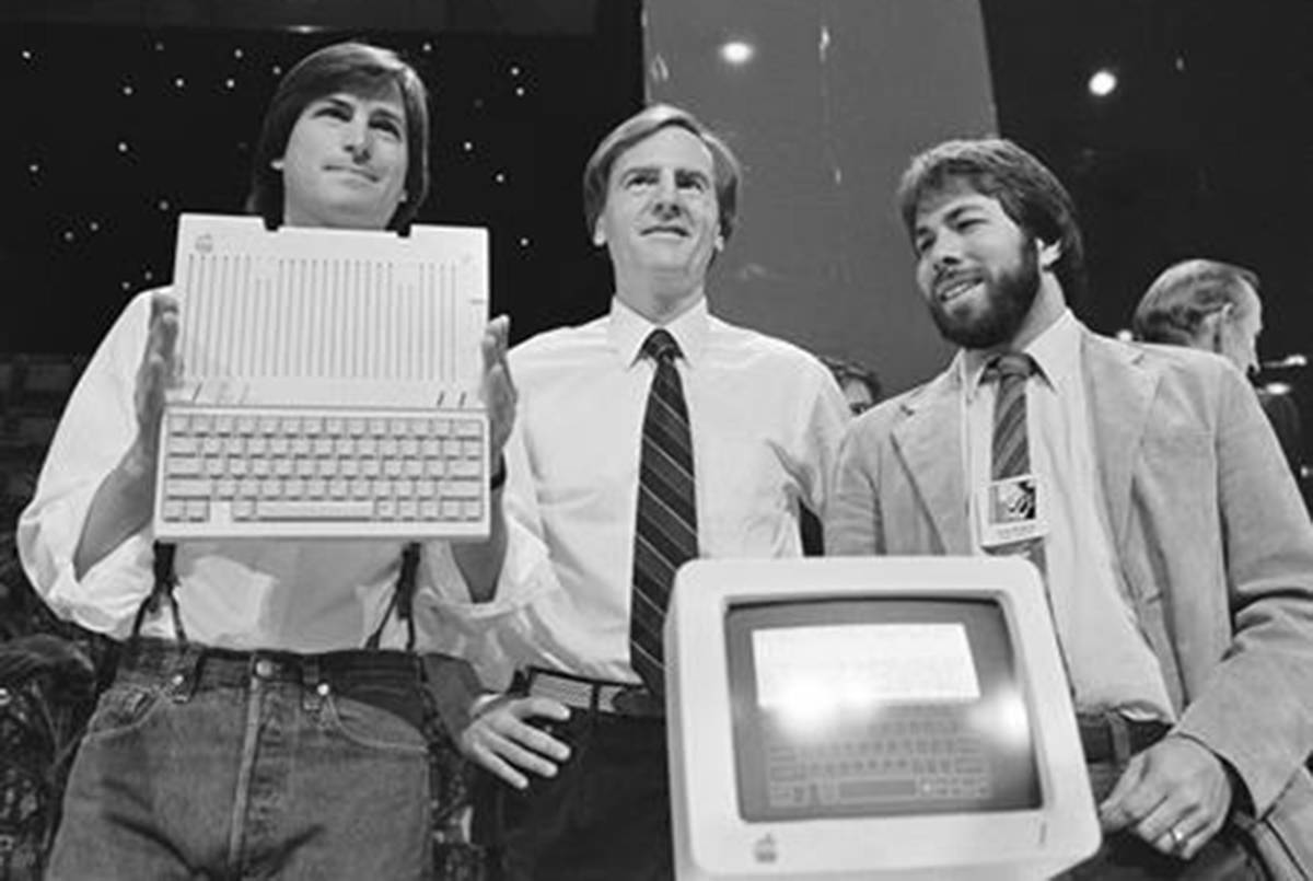 FILE - In this April 24, 1984 file photo, Steve Jobs, left, chairman of Apple Computers, John Sculley, center, president and CEO, and Steve Wozniak, co-founder of Apple, unveil the new Apple IIc computer in San Francisco, Calif. Apple has become the world‚Äôs first company to be valued at $1 trillion, the financial fruit of tasteful technology that has redefined society since two mavericks named Steve started the company 42 years ago. (AP Photo/Sal Veder, File)