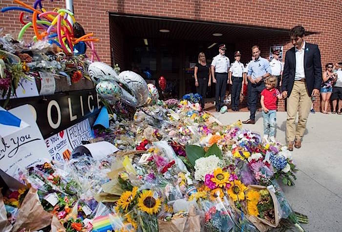 Prime Minister Justin Trudeau, accompanied by his four-year-old son Hadrien and Fredericton MP Matt DeCourcey, left, heads past the tribute after placing flowers outside the police station in Fredericton on Sunday, Aug. 12, 2018. Two city police officers were among four people who died in a shooting in a residential area on the city’s north side. THE CANADIAN PRESS/Andrew Vaughan