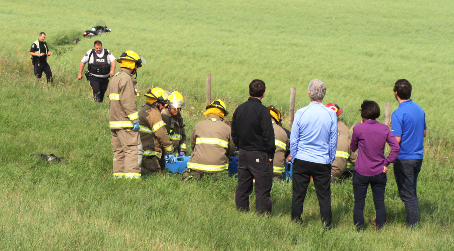 Members of the Ponoka Integrated Traffic Unit investigate a single scooter incident Tuesday afternoon north of Ponoka on Highway 2. Here witnesses watch on as members of the Ponoka County East District Fire Department help lift the rider.                                Photo by Jeffrey Heyden-Kaye
