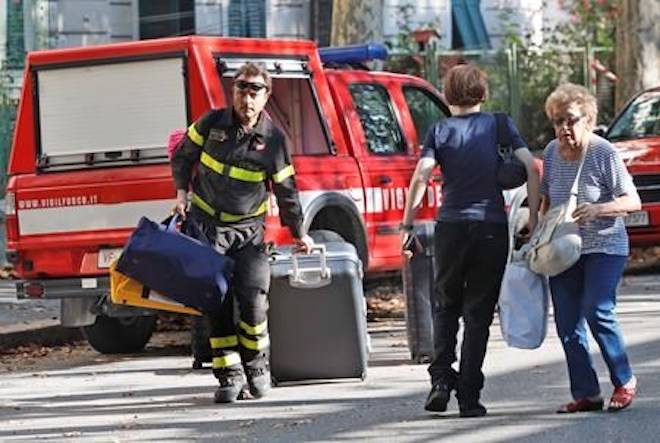 A firefighter pulls a suitcase and carries bags as he accompanies residents to get their belongings from their homes, in Genoa, Italy, Thursday Aug. 16, 2018. (AP Photo/Antonio Calanni)