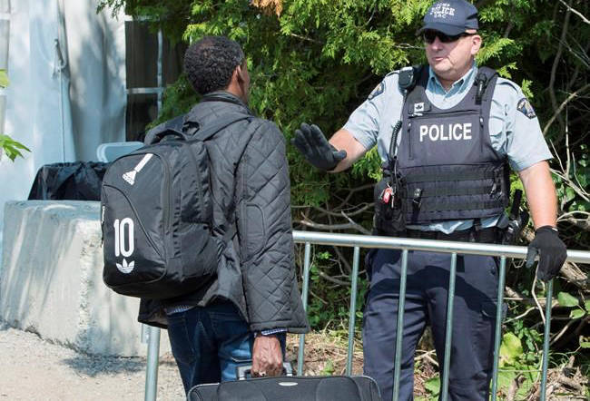 An asylum seekers, claiming to be from Eritrea, is confronted by an RCMP officer as he crosses the border into Canada from the United States Monday, August 21, 2017 near Champlain, N.Y. (Paul Chiasson/The Canadian Press)