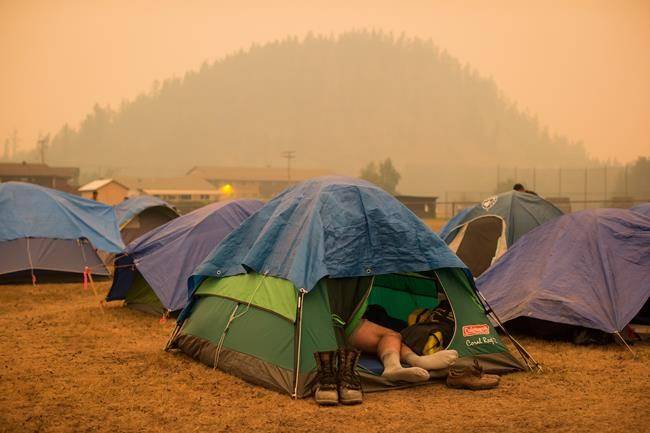Firefighter Raymundo Rosales, of Mexico, lies his tent at a camp of wildfire firefighters and staff at an outdoor sports field, in Fraser Lake, B.C., on Wednesday August 22, 2018. (THE CANADIAN PRESS/Darryl Dyck)
