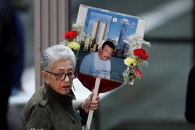 A woman arrives with a sign bearing photo memories for Wilder Gomez at the 17th anniversary of the terrorist attacks on the United States, Tuesday, Sept. 11, 2018, in New York. Gomez, from Colombia, was a bartender at Windows on the World on the 103rd floor of the World Trade Center when it was attacked. (AP Photo/Mark Lennihan)