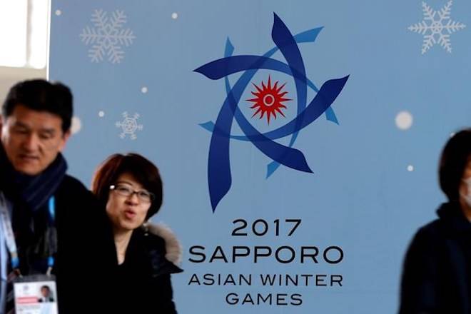 FILE - In this Thursday, Feb. 16, 2017 file photo, people walk by a poster for the Sapporo Asian Winter Games, displayed at the main media center in Sapporo on Japan’s northern island of Hokkaido. (AP Photo/Shuji Kajiyama, File)