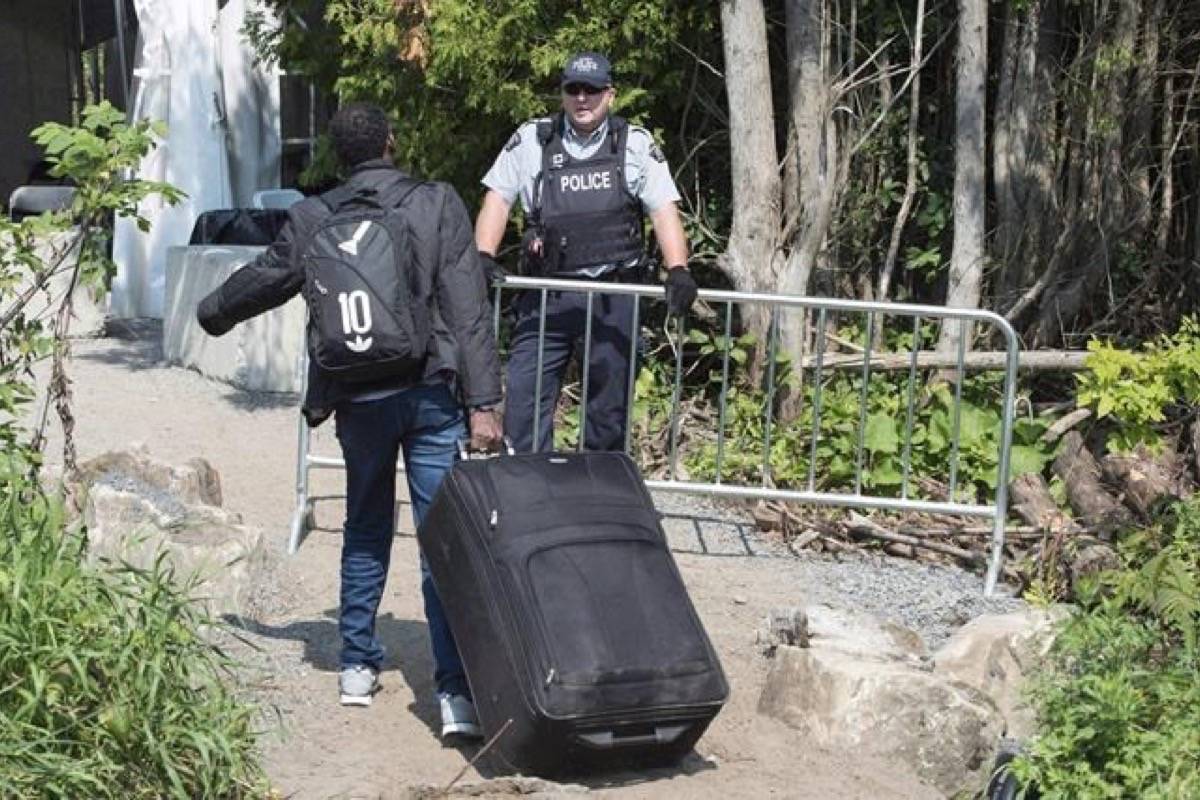 An asylum seeker, claiming to be from Eritrea, is confronted by an RCMP officer as he crosses the border into Canada from the United States on August 21, 2017 near Champlain, N.Y. The number of asylum seekers who crossed into Canada irregularly in August increased slightly over the previous month, but did not reach the record spikes experienced over the summer months last year. (Paul Chiasson/The Canadian Press)