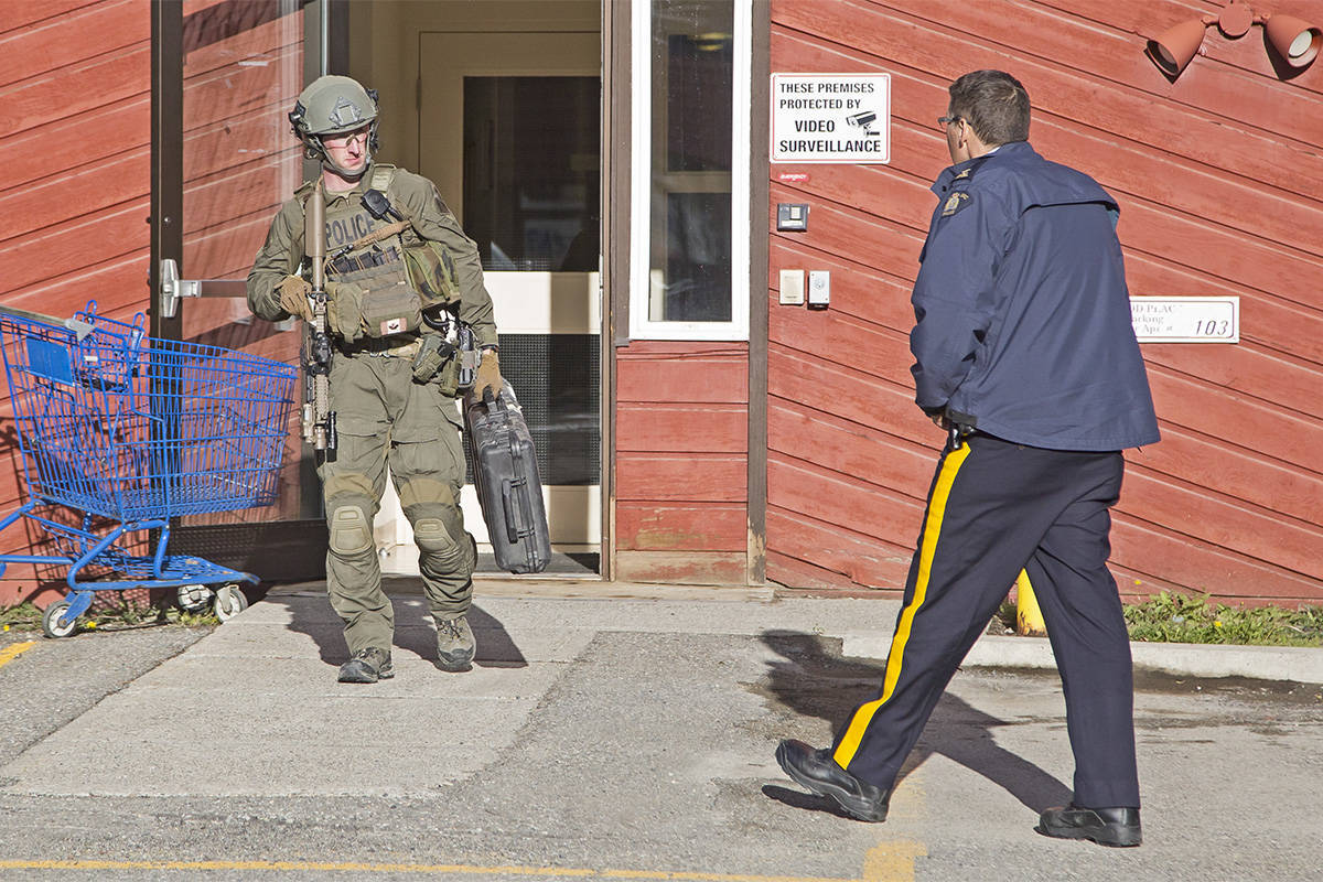 A member of the Yukon RCMP emergency response team, left, and another officer talk after the arrest of Leon Nepper in Whitehorse on Sept. 13. Nepper is now charged with attempted murder and aggravated assault for allegedly mailing an exploding package to his brother. (Crystal Schick/Yukon News)