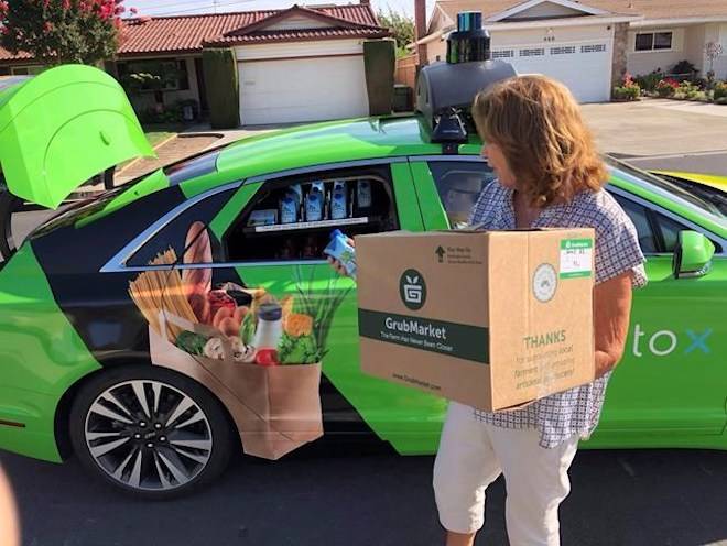 Customer Maureen Blaskovich grabs a coconut water from the backseat window of a self-driving car, a Lincoln MKZ outfitted with technology by AutoX, in San Jose, Calif. on Aug. 29, 2018. Ryan Nakashima / THE ASSOCIATED PRESS