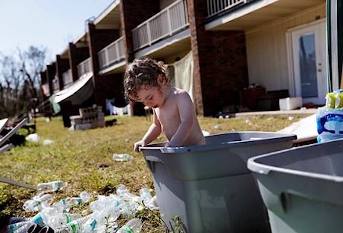 Gaige Williams, 2, cools off in a storage container outside the damaged motel where he lives with his family in the aftermath of Hurricane Michael in Panama City, Fla., Tuesday, Oct. 16, 2018. Many residents rode out the storm and have no place to go even though many of the rooms are uninhabitable. (AP Photo/David Goldman)