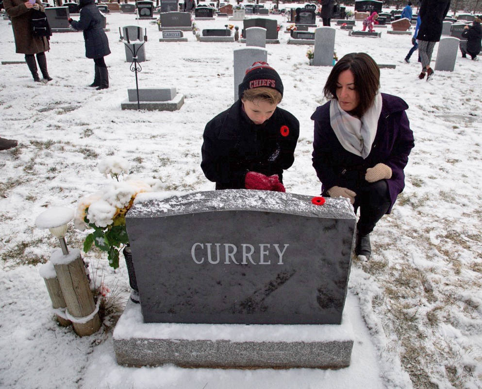 Matthew Morrow placed a poppy on a headstone at Alto Reste Cemetery on Tuesday morning as his mother Keely Morrow watched on. Robin Grant/Red Deer Express