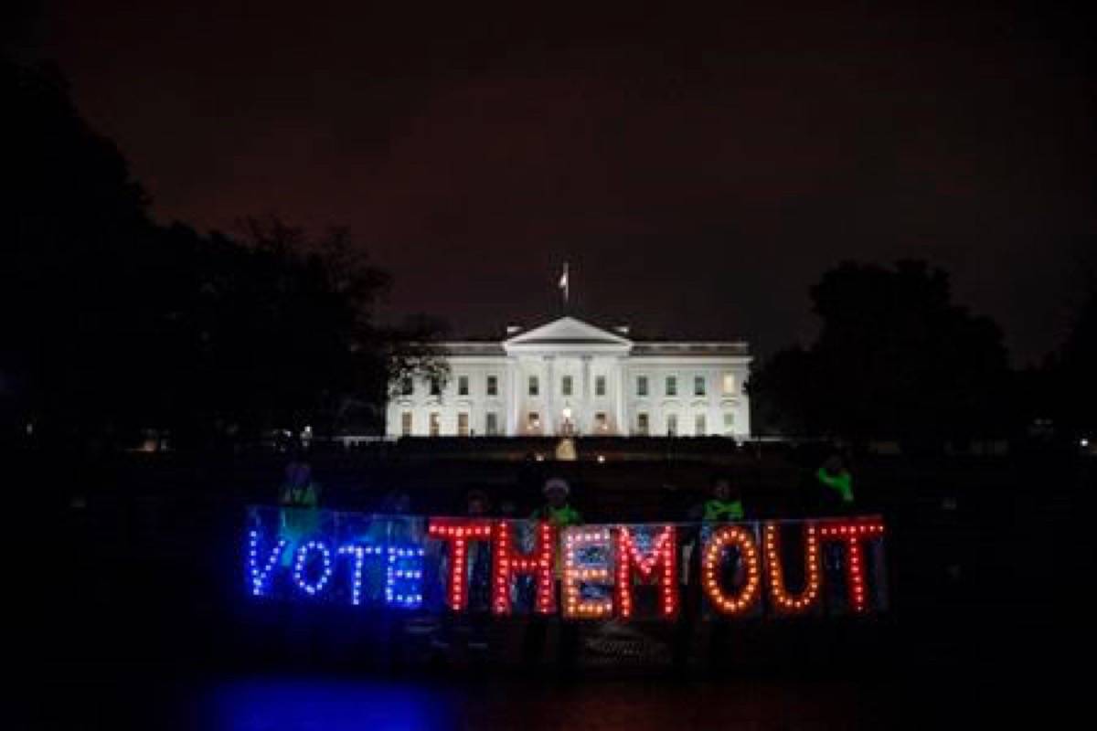 A group of people hold up a sign that reads “Vote Them Out” as they protest in front of the White House the night before midterm election voting begins, Monday, Nov. 5, 2018, in Washington. (AP Photo/Andrew Harnik)