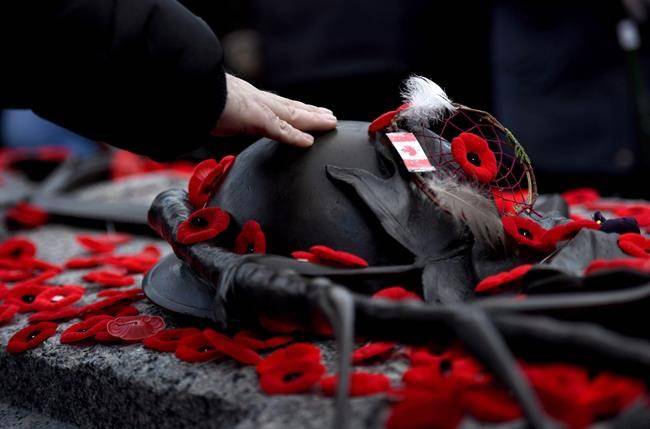 A man touches the helmet on the Tomb of the Unknown Soldier after laying a poppy following the National Remembrance Day Ceremony at the National War Memorial in Ottawa on Saturday, Nov. 11, 2017. (THE CANADIAN PRESS/Justin Tang)