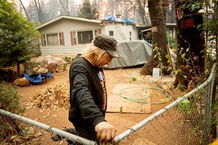 Jimmy Clements, who stayed at his home as the Camp Fire raged through Paradise, Calif., leans against his fence, Sunday, Nov. 11, 2018. Clements, whose home stands among destroyed residences, said he built an FM radio out of a potato and wire to keep up with news about the fire. (AP Photo/Noah Berger)