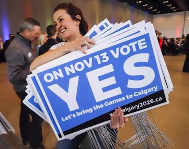 Tabetha Boot carries lawn signs during a rally in support of the 2026 Winter Olympic bid in Calgary, Alta., on November 5, 2018. THE CANADIAN PRESS/Jeff McIntosh