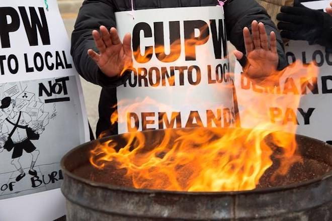 Striking Canada Post workers keep their hands warm as they picket at the South Central sorting facility in Toronto on Tuesday, November 13, 2018. THE CANADIAN PRESS/Frank Gunn