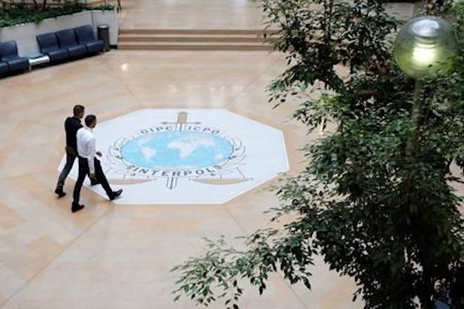 FILE - In this Nov.8, 2018 file photo, people walk on the Interpol logo of the international police agency in Lyon, central France. (AP Photo/Laurent Cipriani, File)