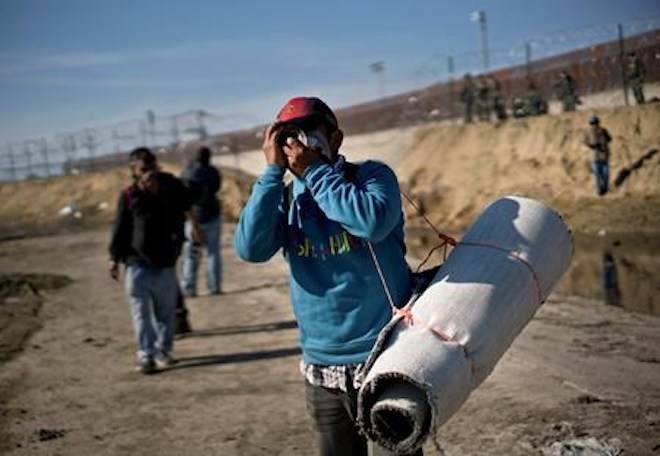 A migrant carrying a roll of carpet wipes his face after U.S. border agents fired tear gas at a group of migrants who had pushed past Mexican police at the Chaparral border crossing in Tijuana, Mexico, Sunday, Nov. 25, 2018. (AP Photo/Ramon Espinosa)