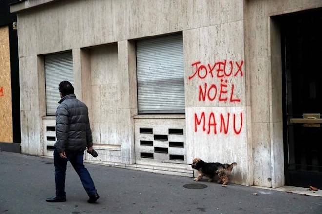 A man walks his dog past a tag reading : Happy Christmas Manu, referring to French President Emmanuel Macron, in Paris, Sunday, Dec. 9, 2018. (AP Photo/Christophe Ena)