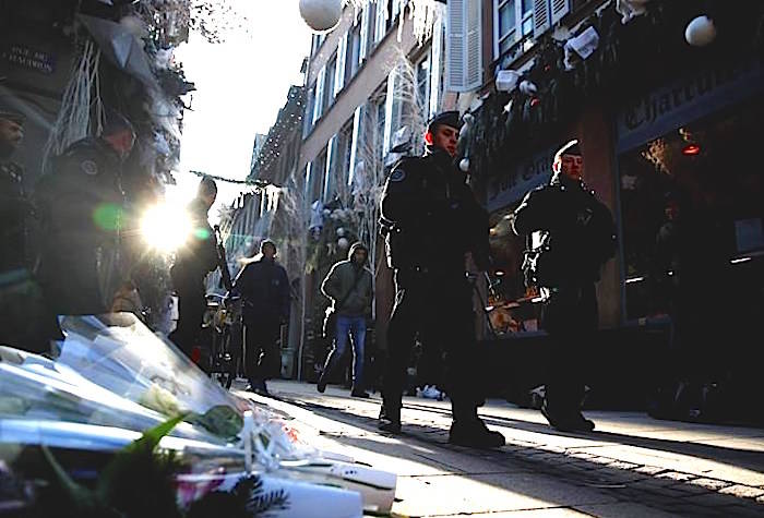 French police officers patrol in the streets front of flowers to pay respects of the victims following an attack killing three persons and wounding at least 13, in Strasbourg, eastern France, Thursday, Dec. 13, 2018. (AP Photo/Christophe Ena)