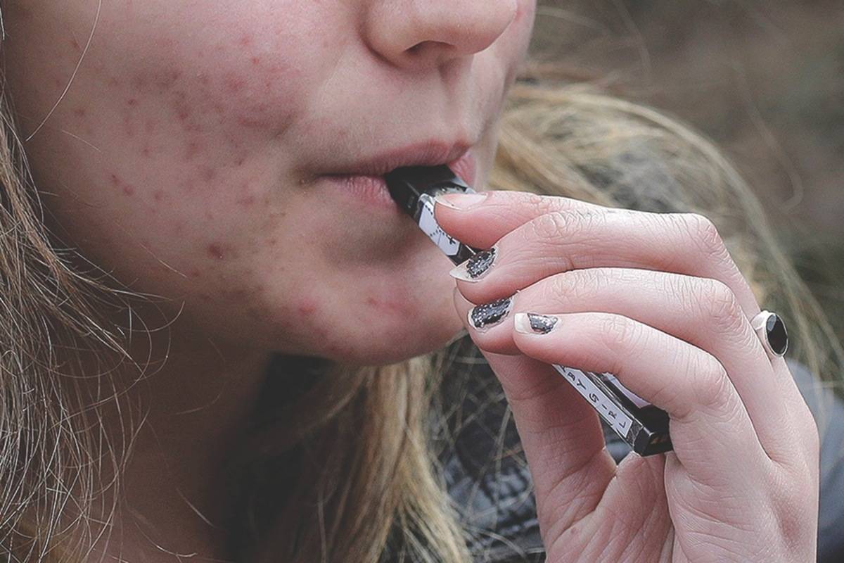 A high school student uses a vaping device near a school campus. File photo by THE ASSOCIATED PRESS