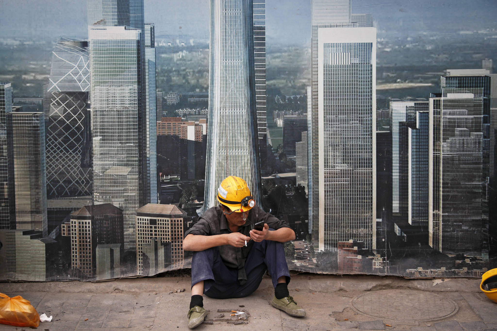 FILE- In this Sept. 19, 2018, file photo a worker browses his smartphone outside a construction site wall depicting the skyscrapers in the Chinese capital at the Central Business District in Beijing. After galloping along for the past two years, the global economy is showing signs of weakening, with the United States, China and Europe all facing the rising threat of a slowdown. Few economists foresee an outright global recession within the next year. But the synchronized growth that powered most major economies since 2017 appears to be fading. (AP Photo/Andy Wong, File)