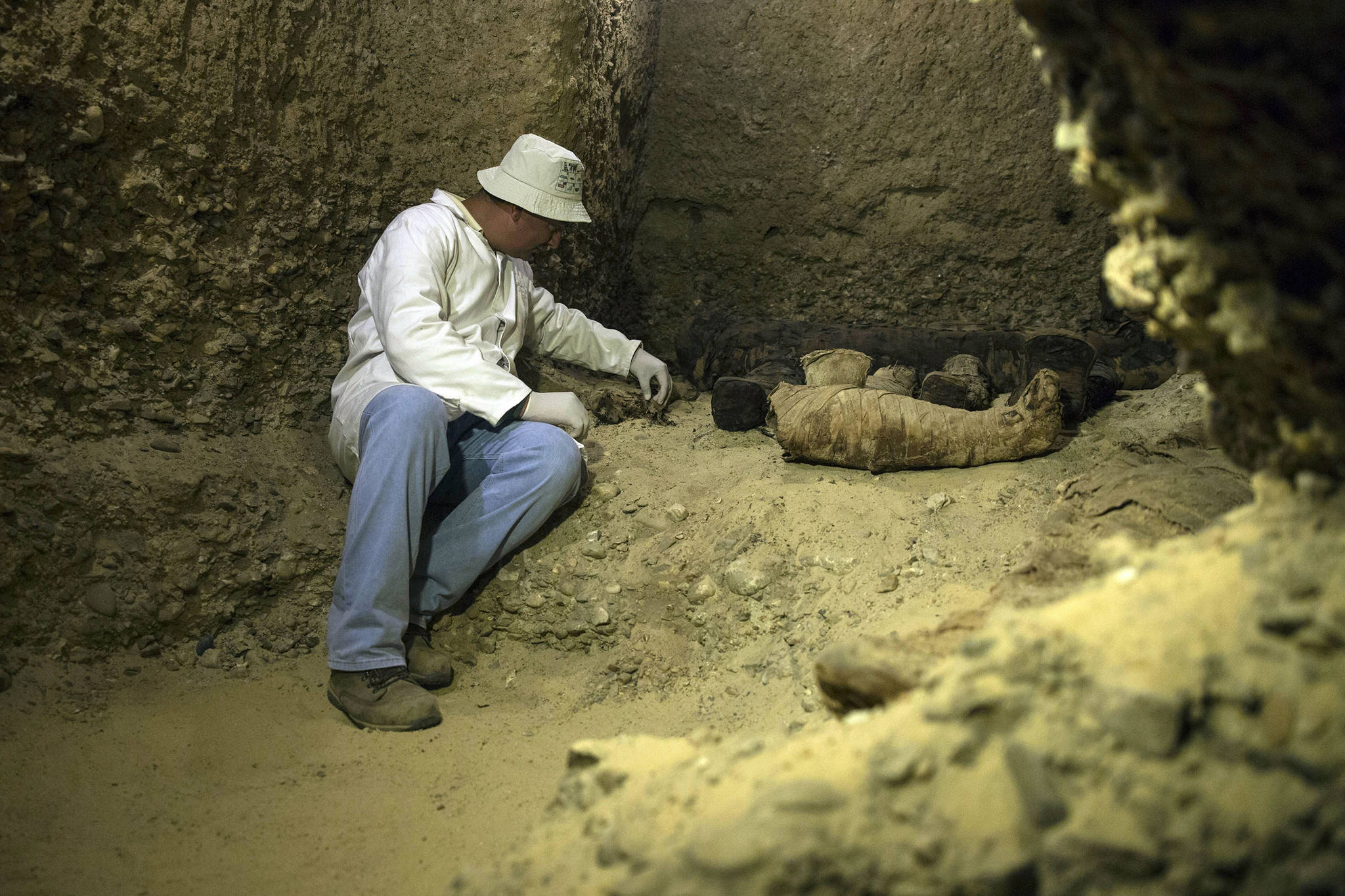 An archeologist looks at mummies discovered in the desert province of Minya, south of Cairo, Egypt, Saturday, Feb. 2, 2019. On Saturday Egypt announced that it found a number of ancient burial chambers cut in rock, carrying about 40 mummies that are in good shape, along with pottery, papyri and exquisite mummy cases. Officials told reporters at the site that the chambers, which were cut out of rock, belonged to a middle-class family that probably lived during the Ptolemaic, early Roman or Byzantine period. (AP Photo/Roger Anis)