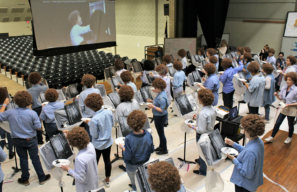 Madison Middle School art students filled the auditorium stage to paint along to Bob Ross, shown on the screen, on Flash Bob Flash Mob Day on Feb. 7, 2019 in Abilene, Texas The students donned their curliest wigs and painted little trees onto canvases to pay homage to the late painter Bob Ross. Teacher Brady Sloane said the idea came about because she wanted to reward Advanced Placement students who had been stressed out over recent projects and grades. (Greg Jaklewicz/The Abilene Reporter-News via AP)