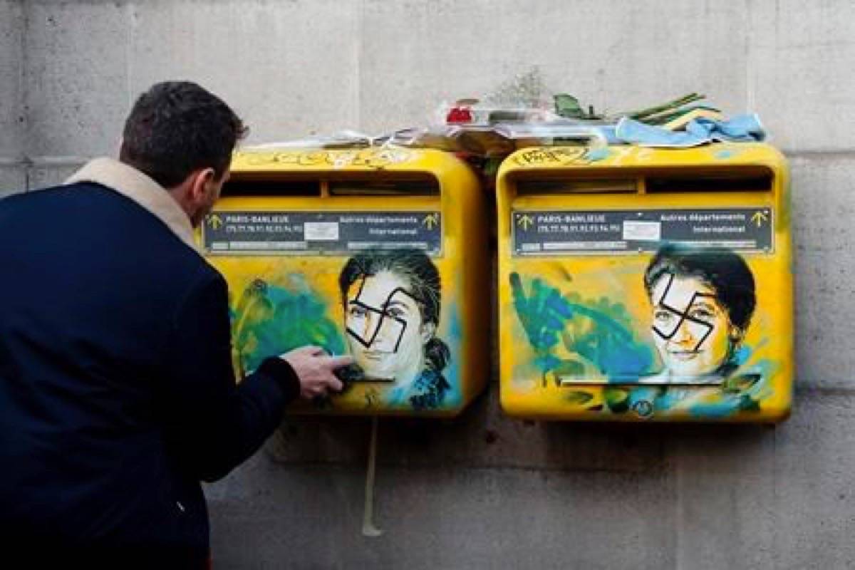 French street artist Christian Guemy, known as C215, cleans the vandalized mailboxes with swastikas covering the face of the late Holocaust survivor and renowned French politician, Simone Veil, in Paris, Tuesday Feb.12, 2019. According to French authorities, the total of registered anti-Semitic acts rose to 541 in 2018 from 311 in 2017, a rise of 74 percent. (AP Photo/Michel Euler)