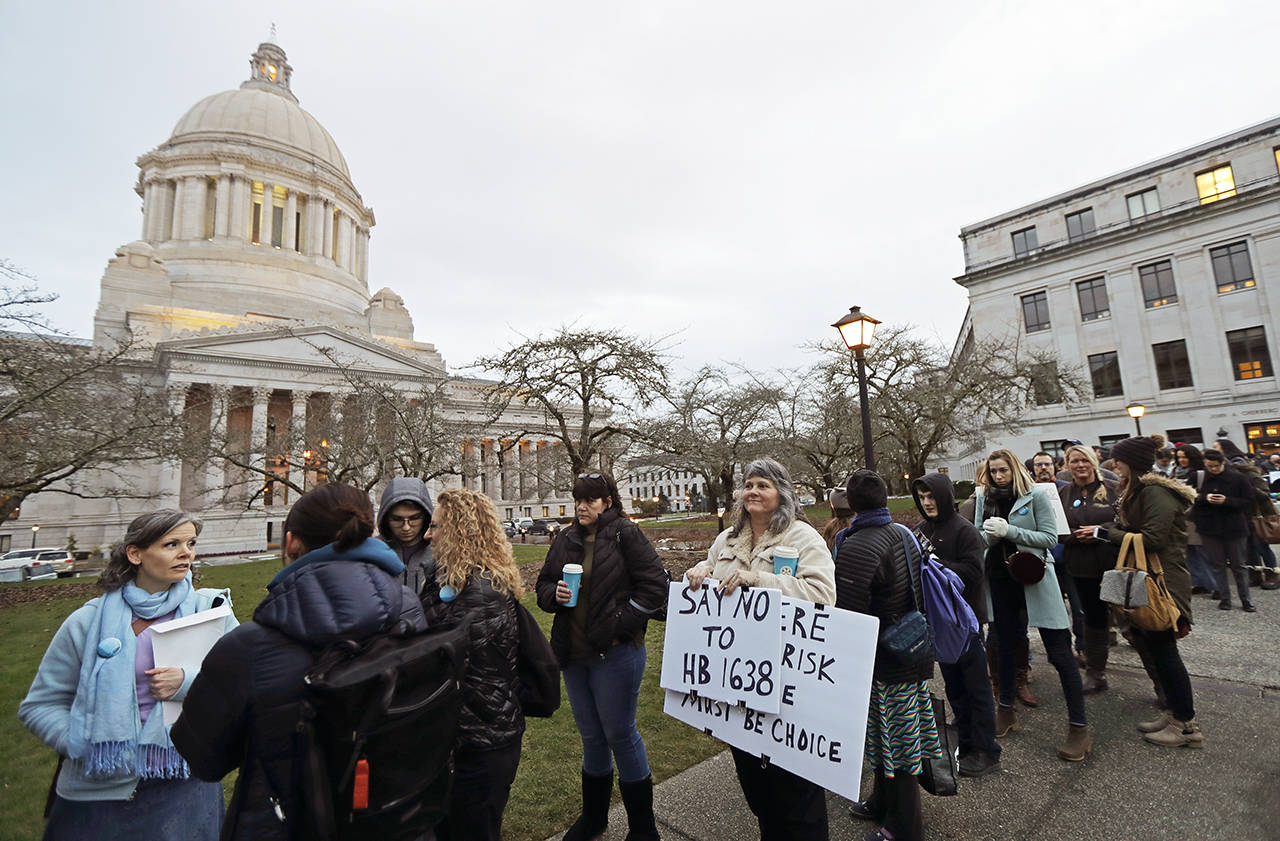 Kebby Johnson, center, of Spokane, Wash., holds a sign that reads "Say No to HB 1638," as she waits in line, Friday, Feb. 8, 2019, to attend a public hearing before the House Health Care & Wellness Committee at the Capitol in Olympia, Wash. Amid a measles outbreak that has sickened people in Washington state and Oregon, lawmakers heard public testimony Friday on a bill that would remove parents’ ability to claim a philosophical exemption to opt their school-age children out of the combined measles, mumps and rubella vaccine. (AP Photo/Ted S. Warren)