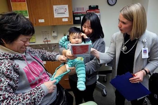 As his mother Wenyi Zhang holds him, one-year-old Abel Zhang looks at the book being given him by Dr. Lauren Lawler, right, as his grandmother Ding Hong helps with his clothes moments after the child received the last of three inoculations, including a vaccine for measles, mumps, and rubella (MMR) (AP Photo/Elaine Thompson)