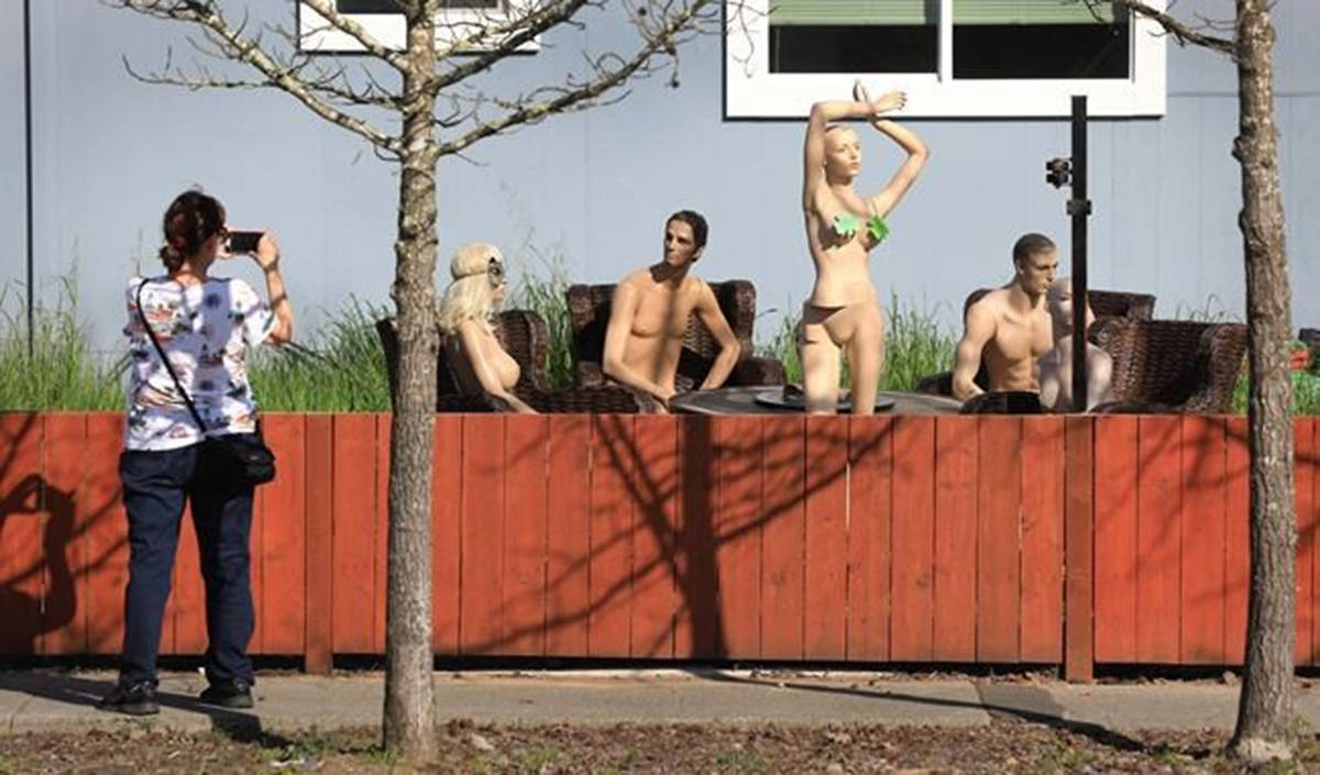 In this photo taken Monday, March 18, 2019, a woman stops to photograph a display of mannequins in Santa Rosa, Calif. Homeowner Jason Winduce set up the display, after a neighbor in the area complained to the city about his six-foot-tall fence. Winduce had to cut the fence to three feet. (Kent Porter/The Press Democrat via AP)